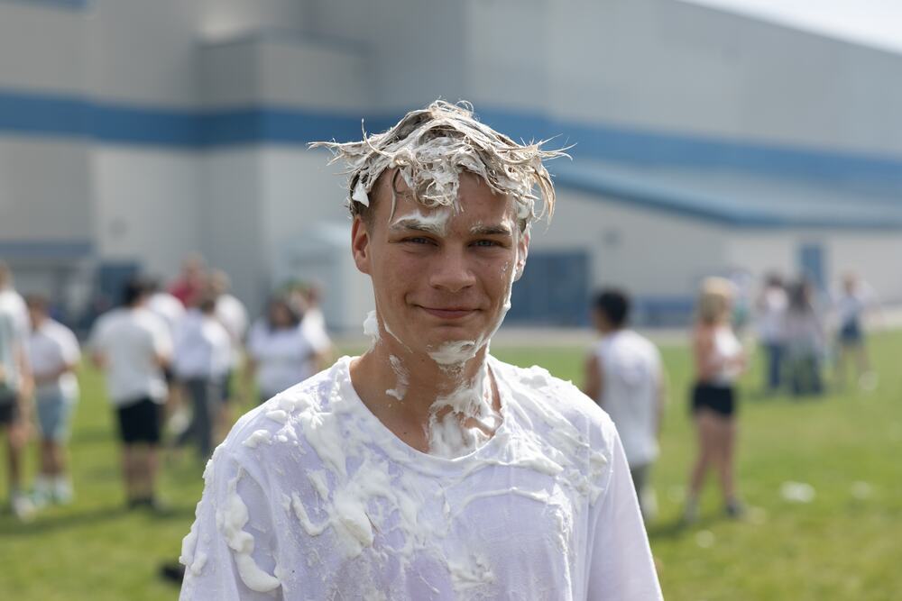 A senior covered head to toe in shaving cream, grinning at the camera on the field.