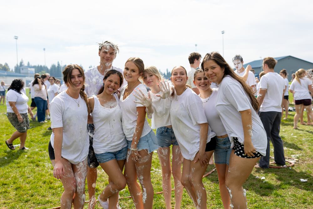 A group of seniors in white T-shirts with their arms around each other on the grass, shaving cream everywhere.