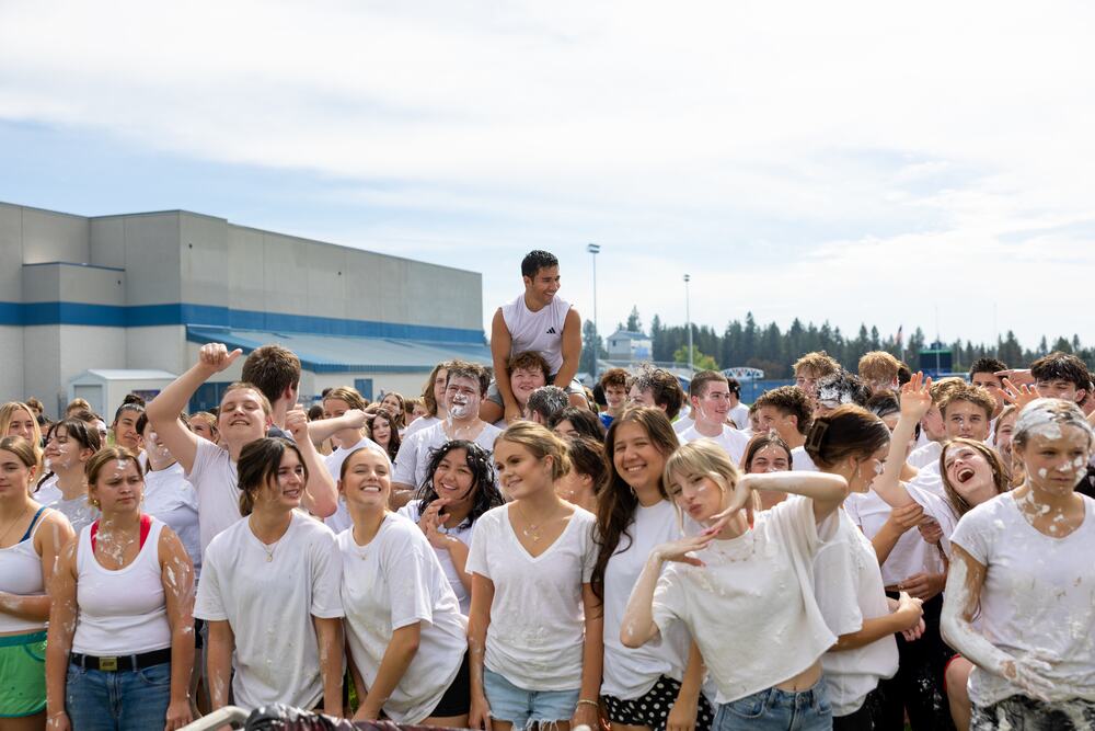 A crowd of seniors in white shirts covered in shaving cream, cheering with one classmate lifted on shoulders behind them.