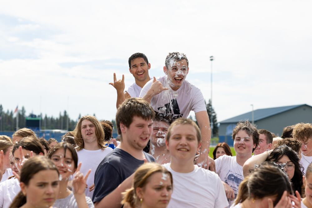 Two seniors lifted above the crowd, one covered head to toe in shaving cream, both throwing their hands up.