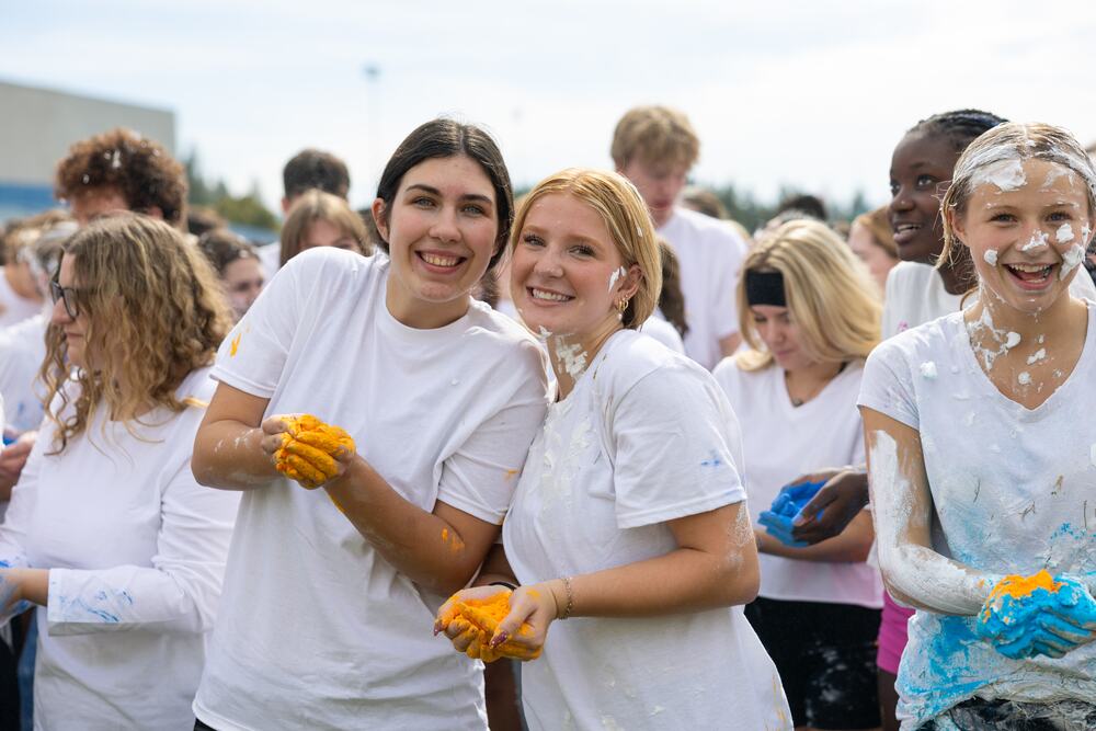 Two seniors in gloves holding handfuls of color powder, ready to go.