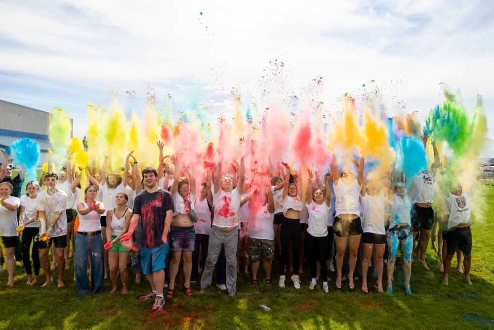 Plumes of yellow, pink and blue powder thrown up over the class against an open sky.