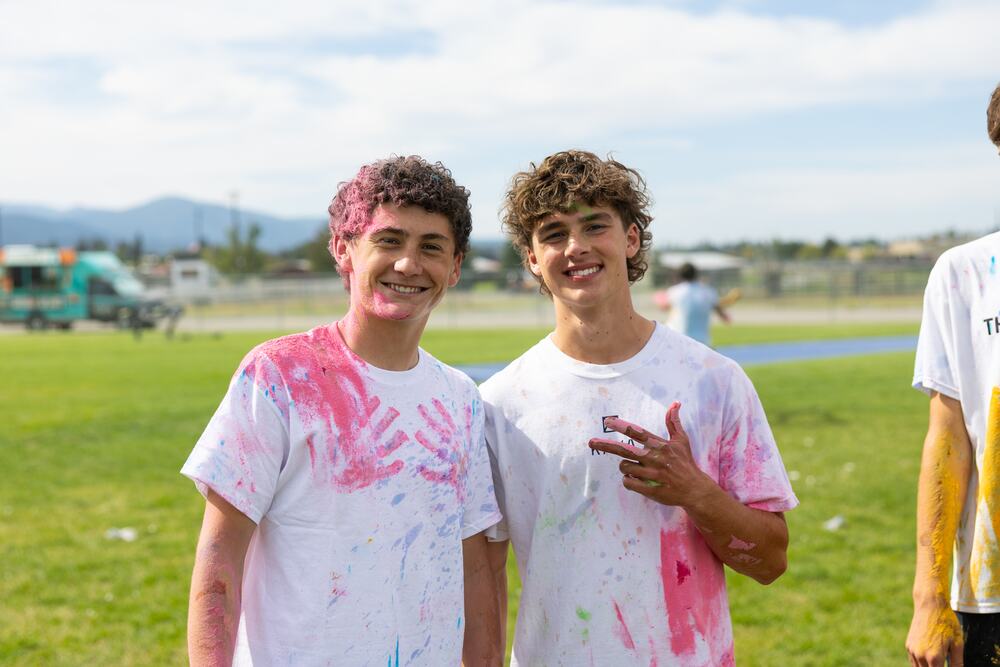 Two seniors covered in pink and blue handprints, grinning at the camera on the field.