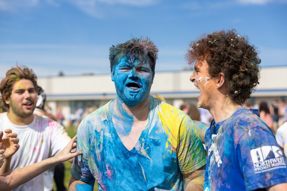 A senior with his whole face and shirt turned blue, laughing with friends.