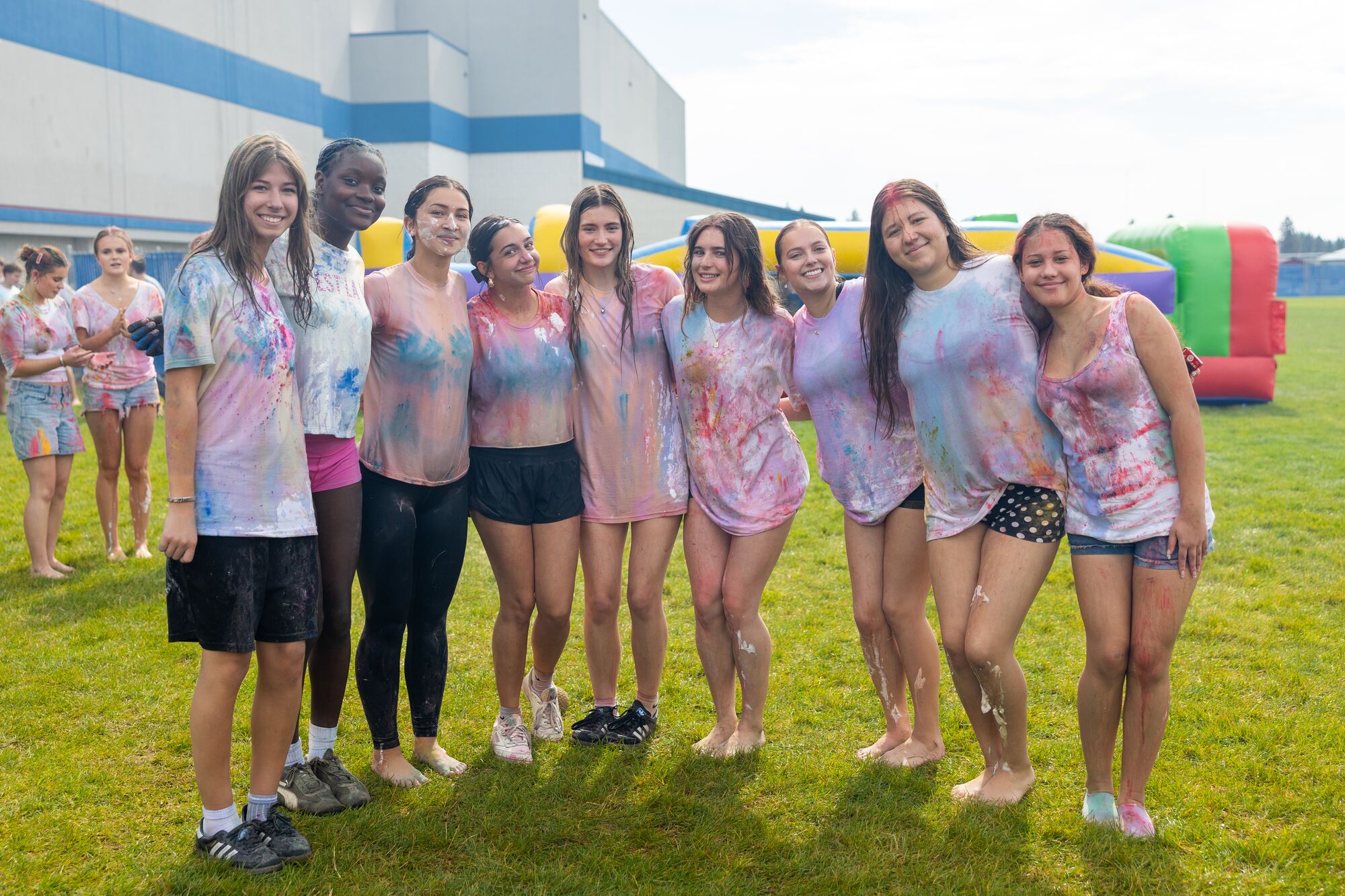 A line of CHS seniors covered in color powder, arms around each other in front of the school at Senior Start