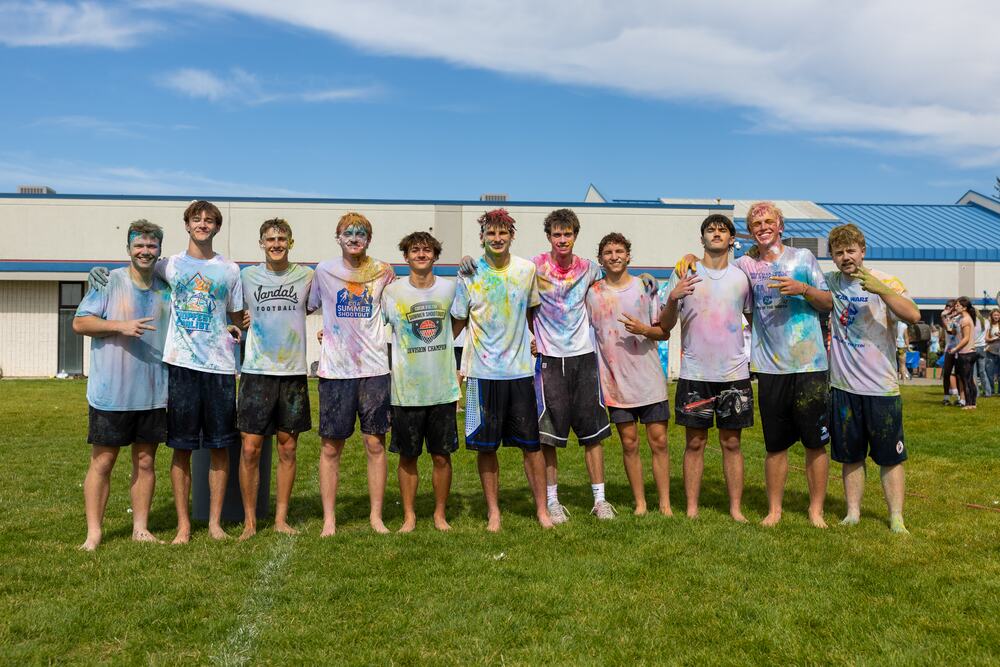 A row of senior boys covered in color, arms around each other in front of the school.
