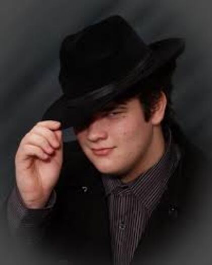 A senior in a wide black hat, lit so most of his face is in shadow