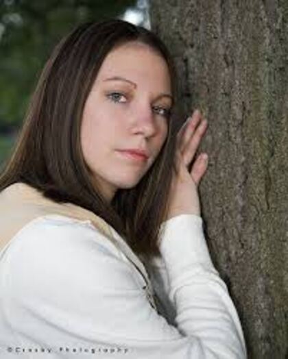 A senior leaning against a tree with her face turned away from the camera